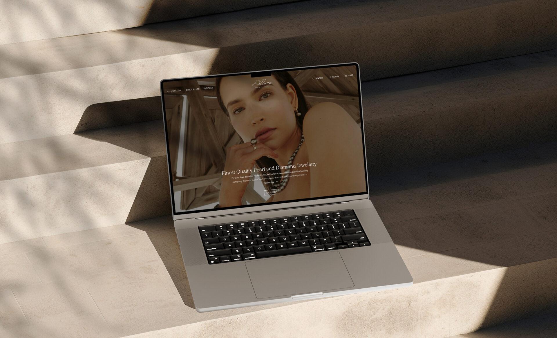 Mockup image of a laptop on concrete stairs, showcasing the home page design of the Allure South Sea Pearls website.