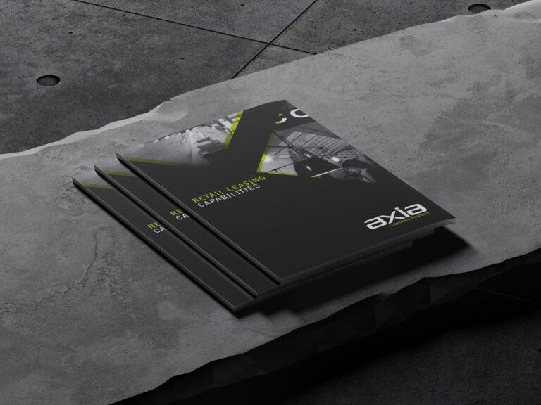 Three booklets stacked on a concrete bench, showing the Axia Corporate Property document design.