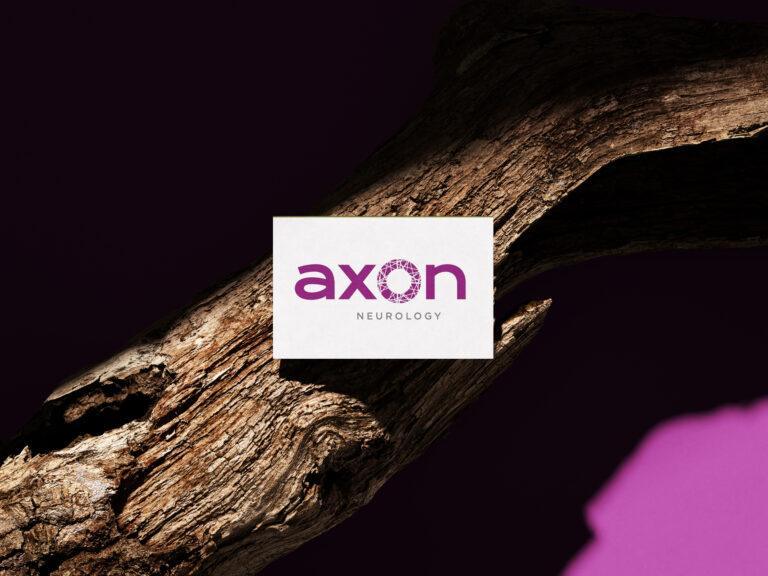 A mockup of a business card lying on top of wood, featuring the Axon Neurology company logo.