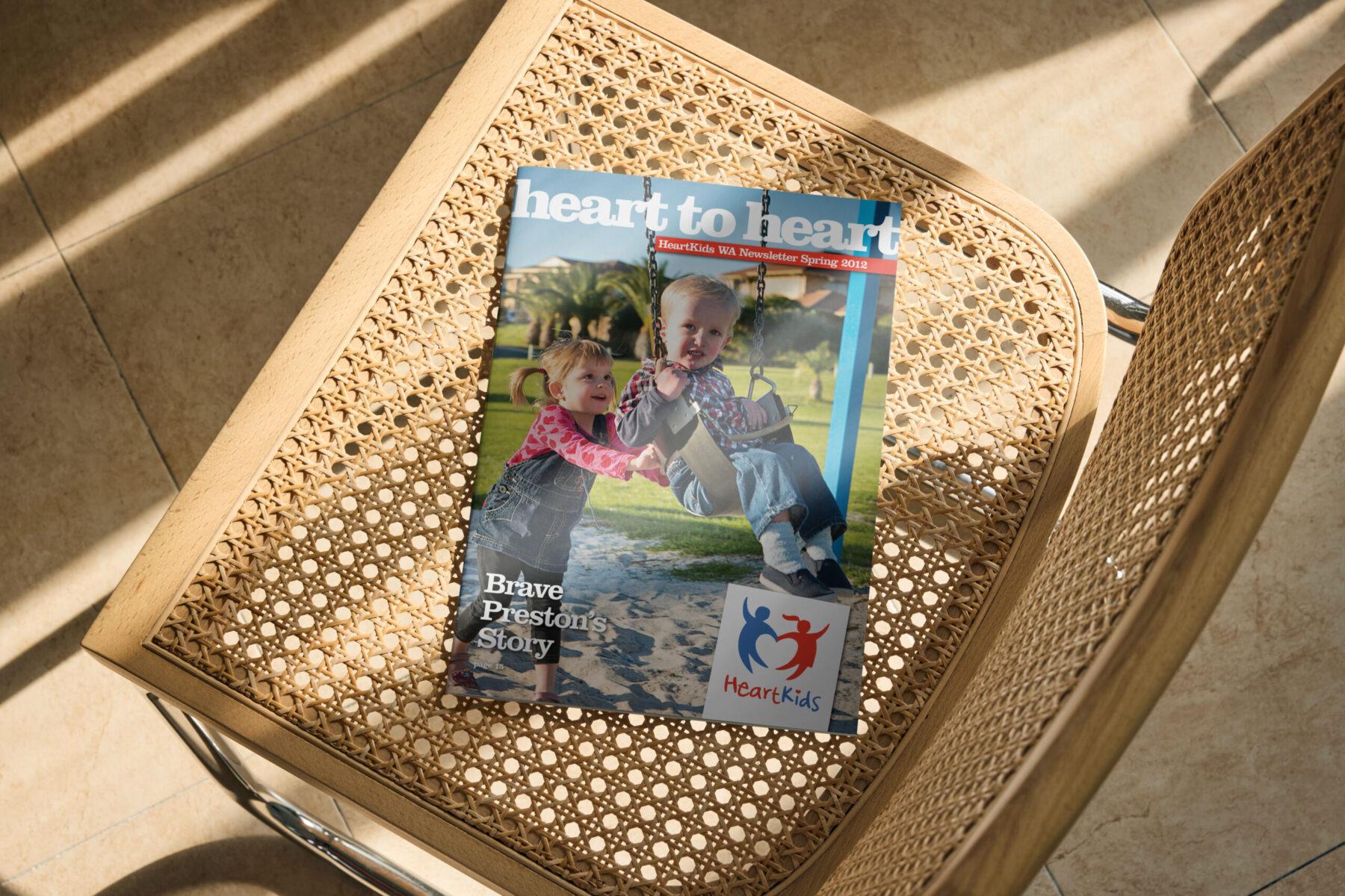 A mockup of a magazine lying on a thatched chair, with the cover design for Heartkids WA.