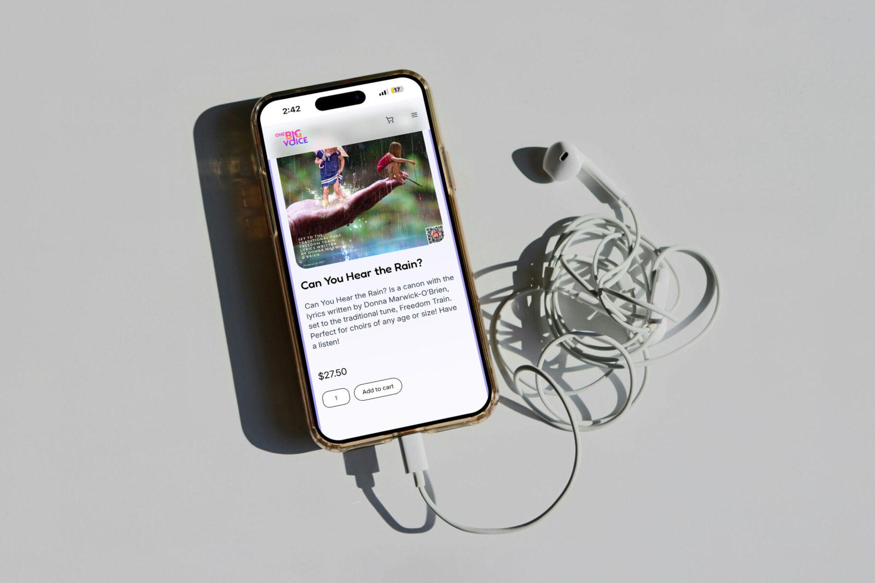 Mobile phone lying flat on ground with One Big Voice's website on screen. Page displayed is a product listing in their music store.