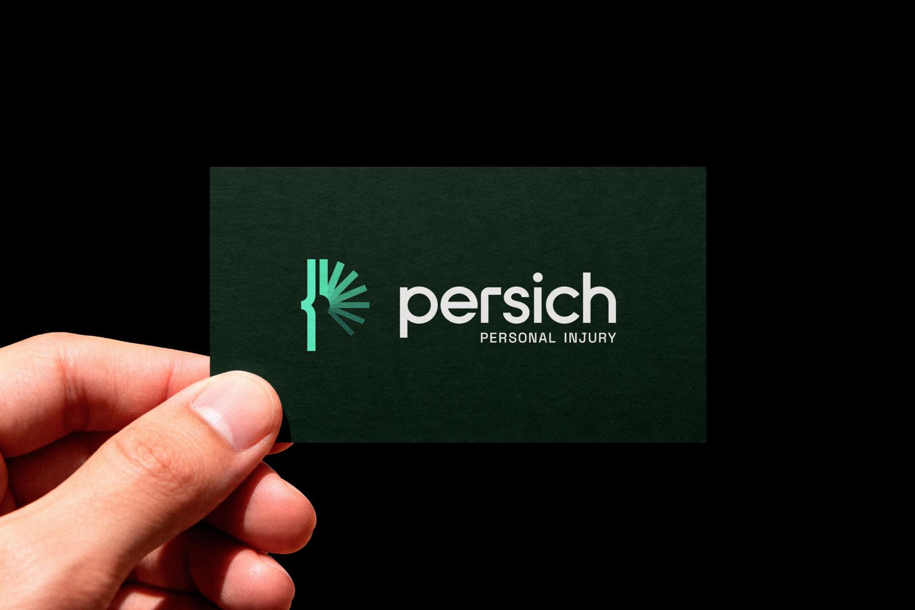 A close-up shot of a hand holding a business card, showing the Persich logo design.