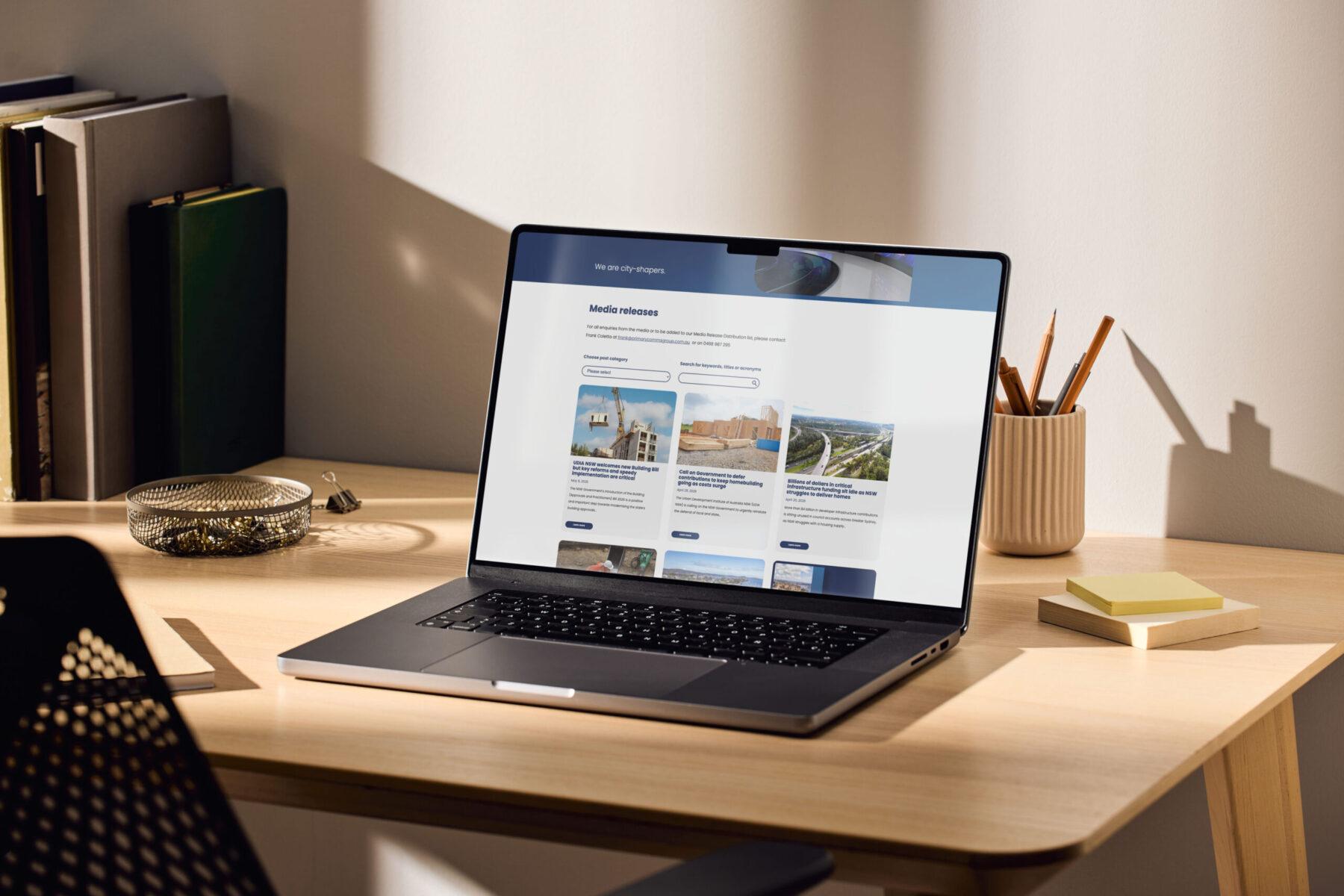 A mockup of a laptop on a desk, displaying an example web page design for the UDIA NSW website.