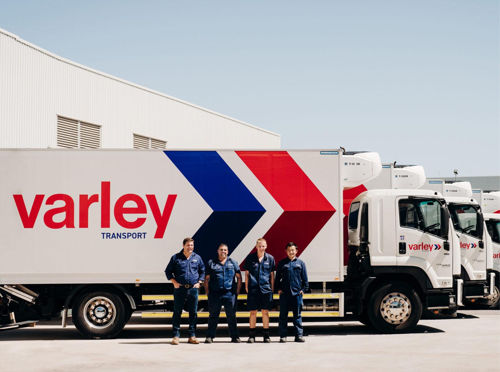 Four men stand in front of a row of industrial trucks with Varley Transport logo and branding on their exteriors.